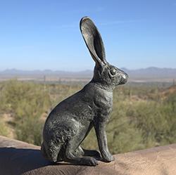 大野兔青铜雕塑坐落在土坯墙上，以沙漠景观和蓝天为背景